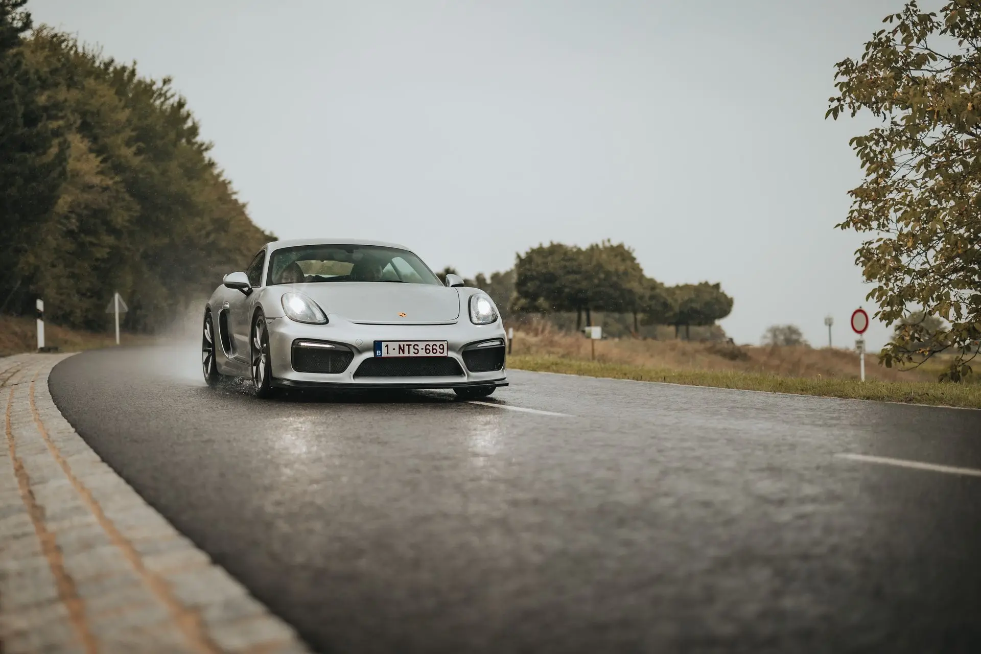 Light gray Porsche Cayman driving in the rain