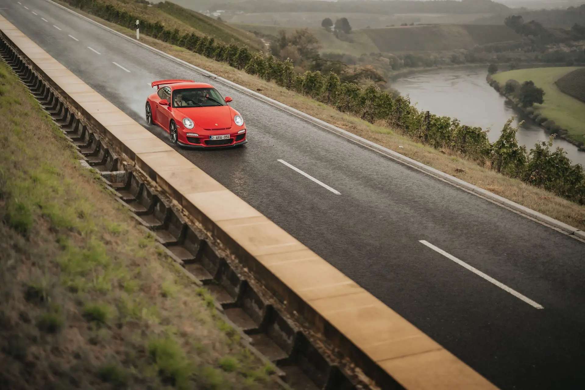 Porsche 911 GT3 driving on wet road with river in the background