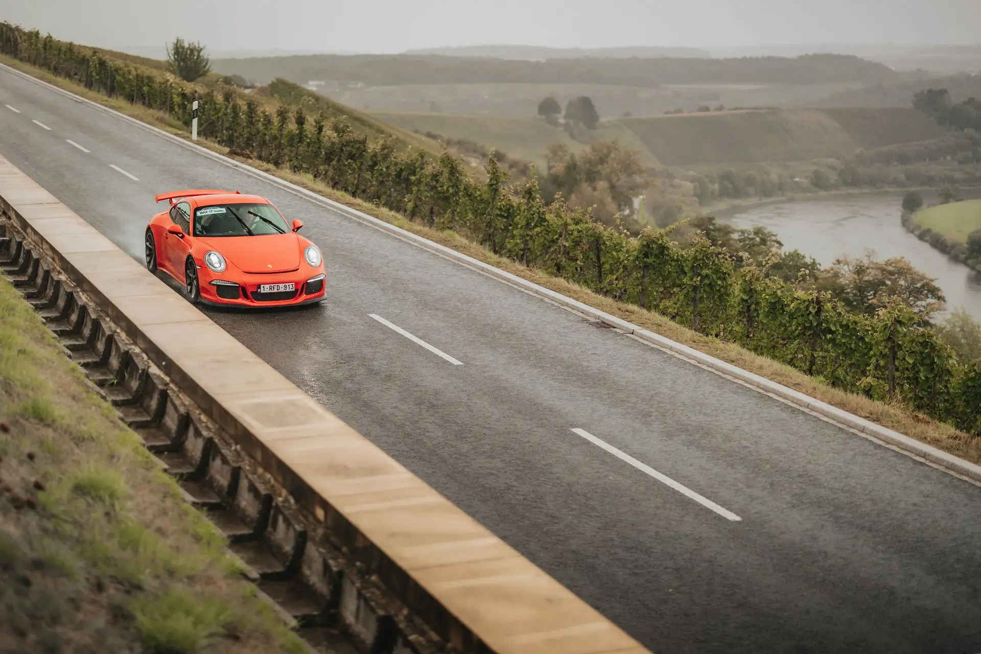 Orange Porsche 911 GT3 driving in the rain on a country road