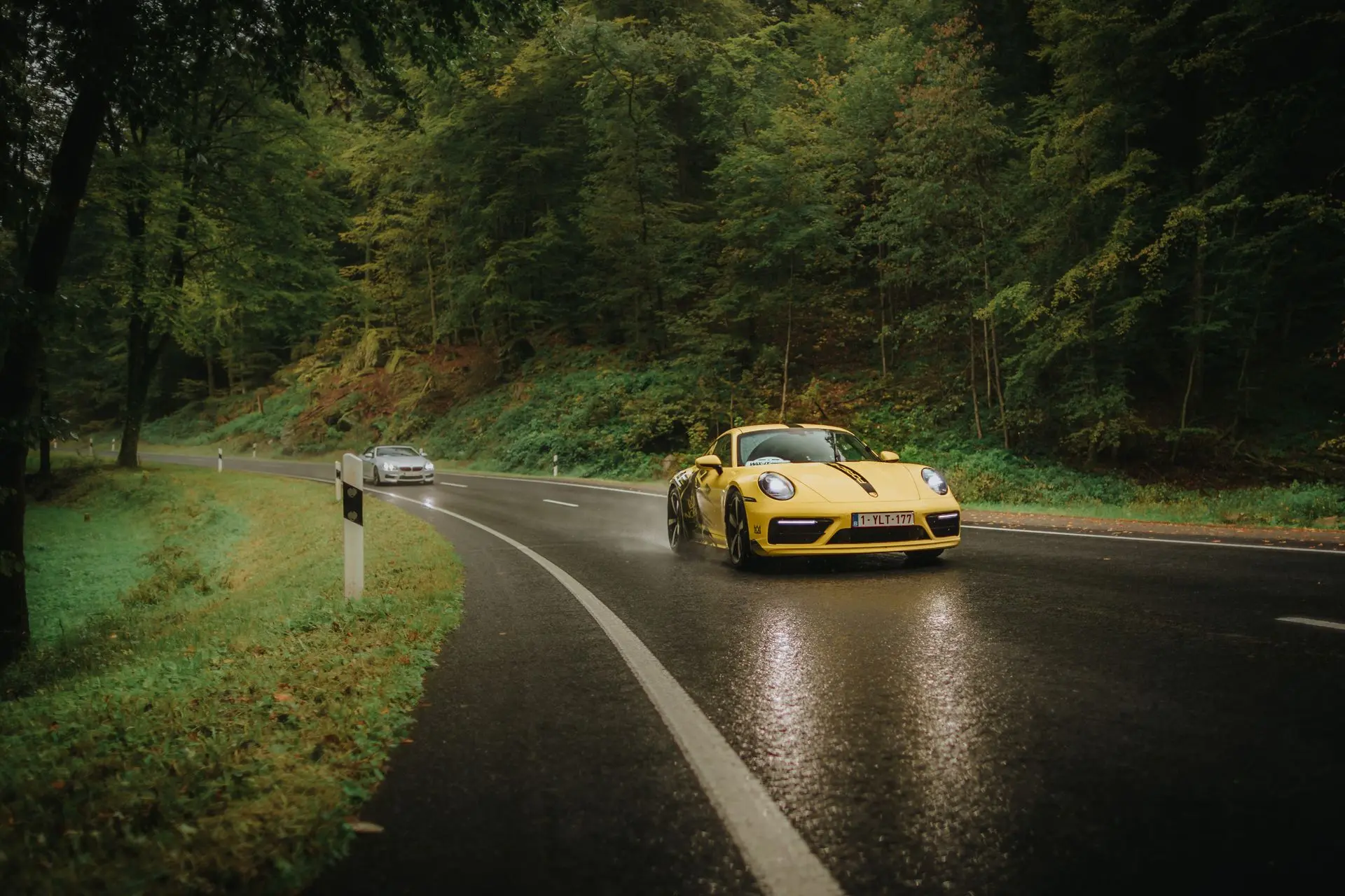 Yellow Porsche 911 with NOBLE branding driving on wet road in rainy forest