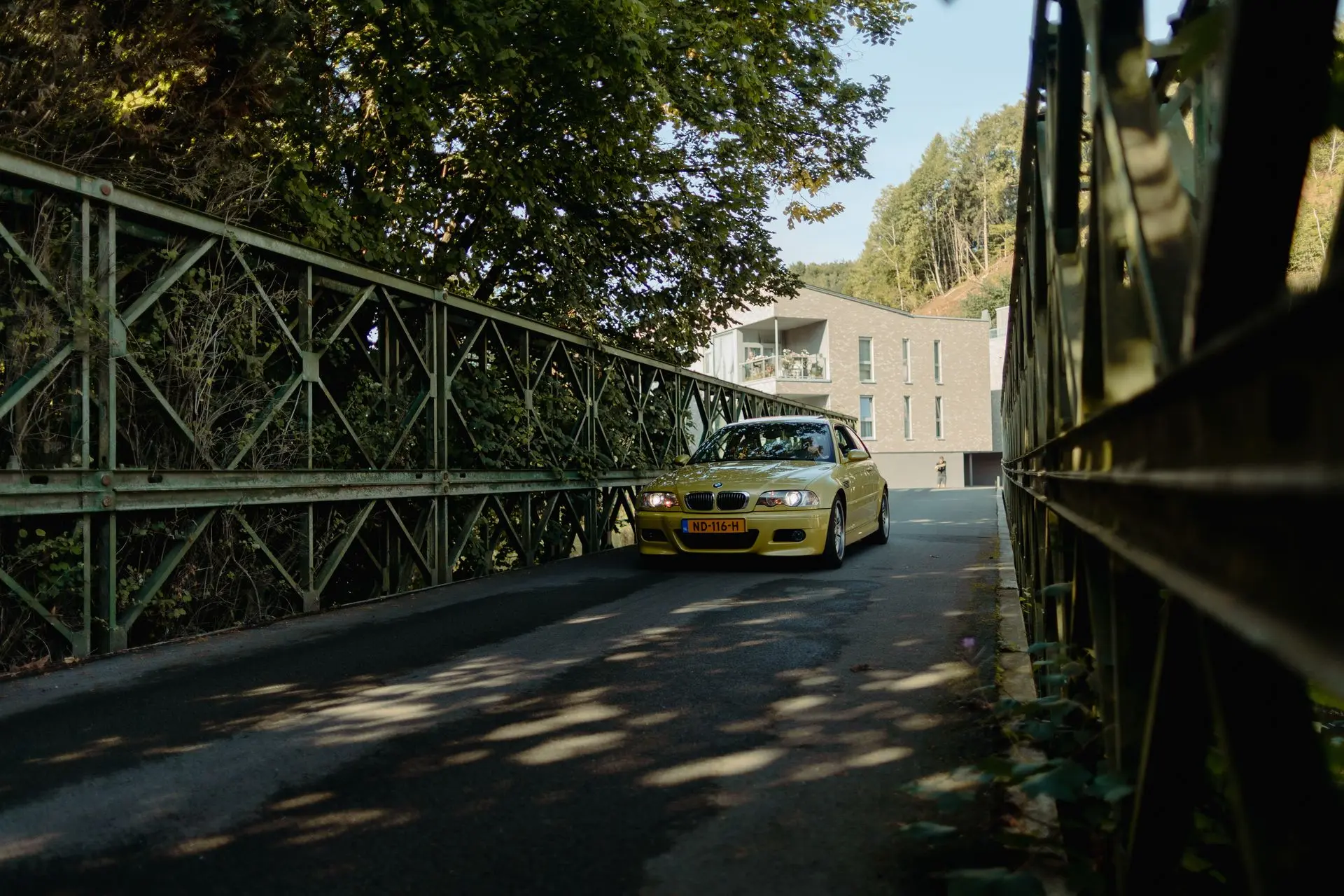 Yellow BMW e46 coupé driving down an old bridge